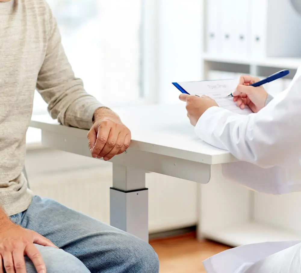 Arzt und Patient besprechen im Sprechzimmer eine bösartige Tumorerkrankung wie Prostatakrebs, der Arzt macht sich Notizen.